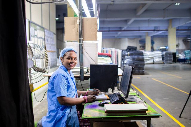 Smiling factory worker using a computer at a production facility — stock photograph